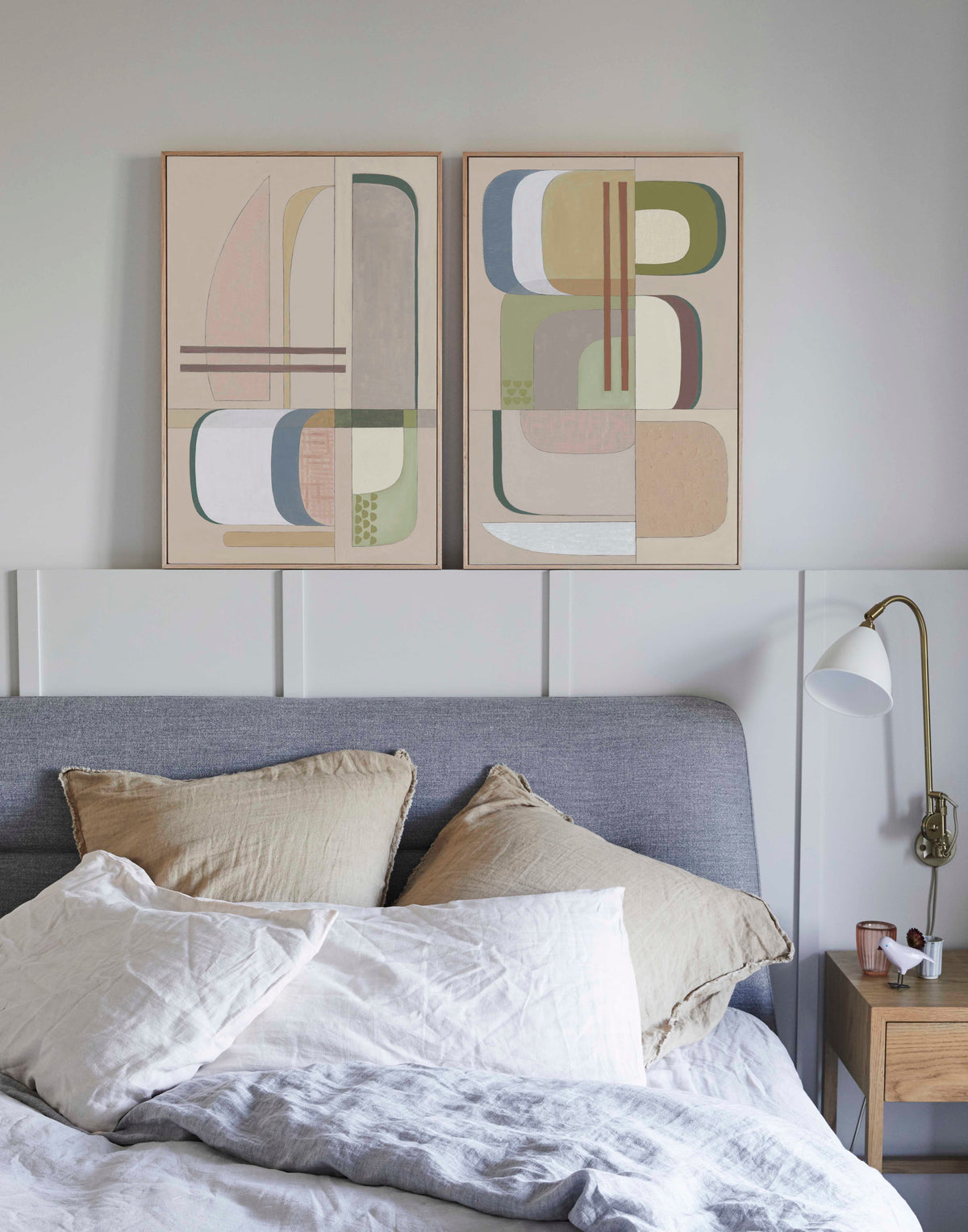 Studio Elwood “Olympia Diptych” — pair of abstract geometric artworks in sage, blush, taupe, and ivory tones, framed in oak and displayed above a serene contemporary bedroom setting with natural linen bedding and soft neutral palette.