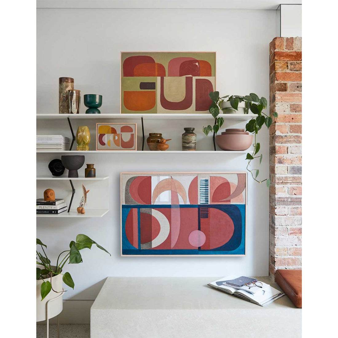 Framed abstract wall art with geometric patterns, featuring arches and curves, in vibrant and neutral colors, displayed on a white wall above a shelf with various decor items.