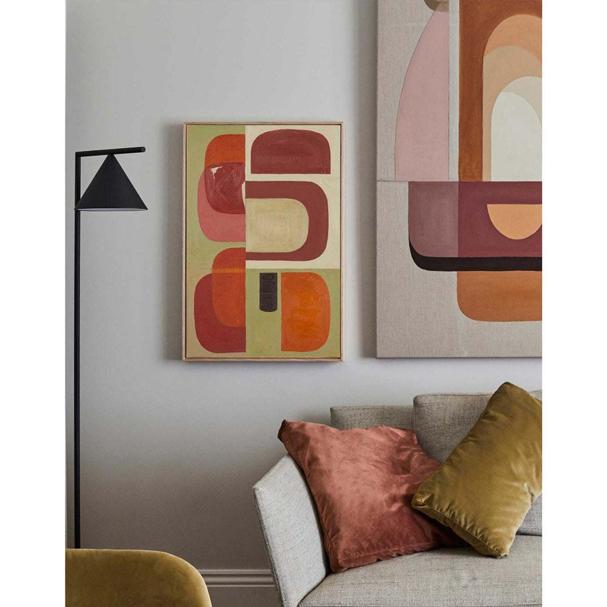 Framed Giclee print with abstract geometric shapes in red, orange, and brown tones, displayed above a sofa with a lamp and a pillow in a living room setting.