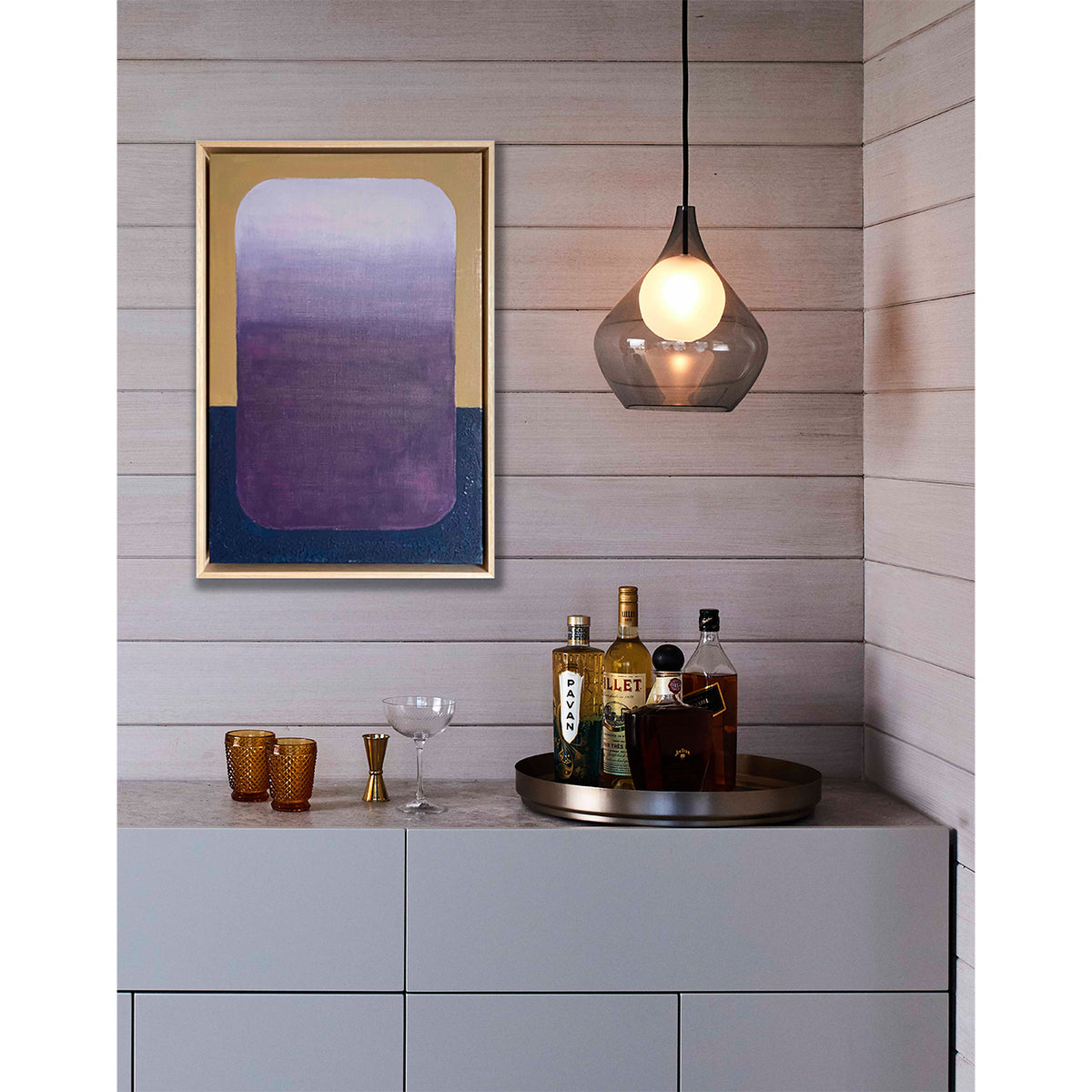 Modern interior with a shelf displaying bottles and glasses, a pendant light, and abstract art on the wall.