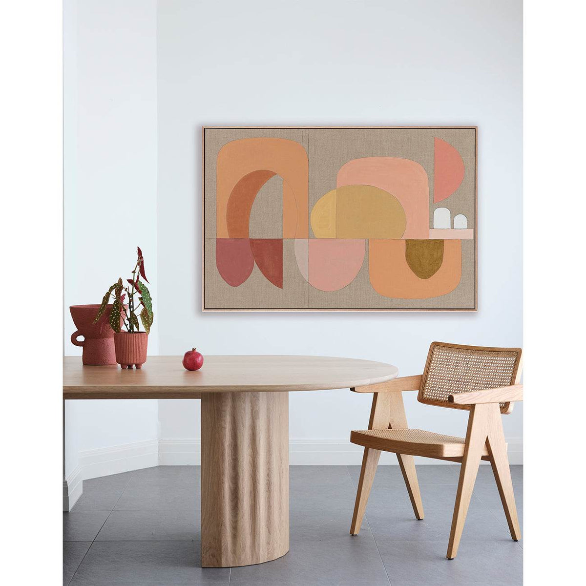 A framed Giclee print featuring geometric shapes in warm colors displayed above a wooden table and a chair in a minimalist interior setting.