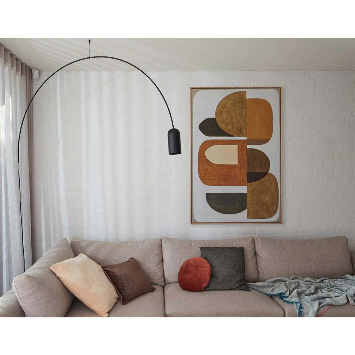 A framed Giclee print featuring geometric shapes in earthy tones, hanging over a sofa with a black pendant light.