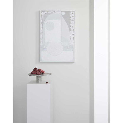 A framed Giclee print on canvas, displaying a geometric pattern with arches and curves, mounted on a white wall above a platform with fruits.