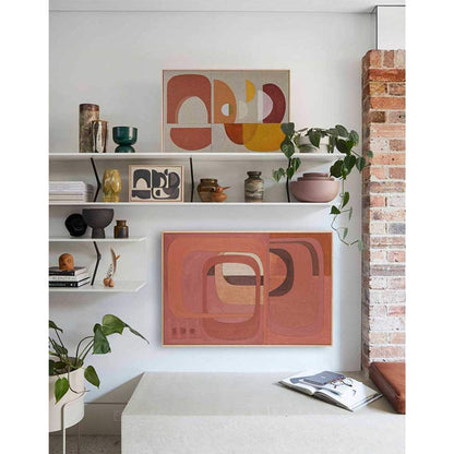Framed Giclee prints featuring geometric shapes in warm orange, terracotta, and pink hues displayed on a shelf above a modern living room setup.